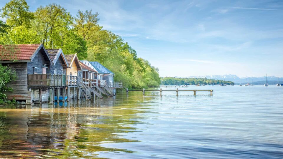 Bunte Hausboote am ruhigen Wasser mit Steg und grünen Bäumen, idyllischer Ort am See.